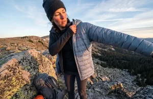 Best Lightweight Down Jackets Worth Buying for Hiking Hiker pausing at ridgeline to pull on lightweight down jacket in cold alpine morning light