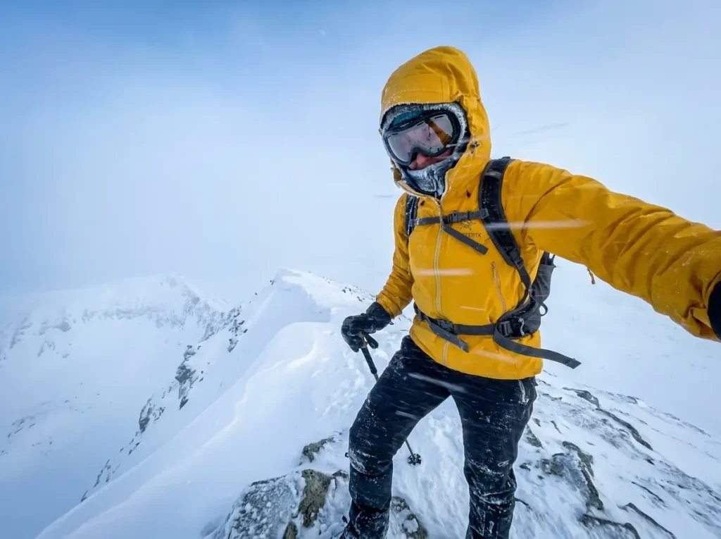 Hiker in hardshell jacket facing blowing snow on an exposed winter ridge
