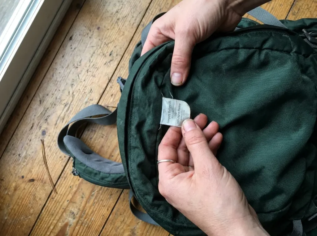 Hands checking the fabric tag inside an older Gregory Baltoro hiking backpack to judge its age