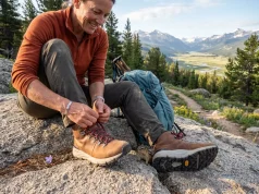6 Best Hiking Boots for Plantar Fasciitis 2026 Hiker lacing up supportive hiking boots on a granite boulder overlooking a mountain valley