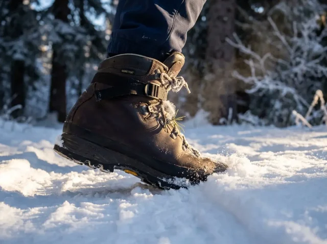 insulated-winter-hiking-boots-hero Close-up of an insulated winter hiking boot stepping into fresh snow on a frozen alpine trail at golden hour