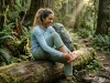 Why Merino Socks Smell Less on Trail (7-Day Field Test) Female backpacker resting on a log removing a hiking boot to reveal a green Darn Tough merino wool sock