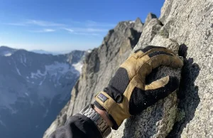 Best Mountaineering Gloves for Class 4 Scramblers Close-up of a scrambler's gloved hand gripping a granite hold during a Class 4 ridge scramble in alpine sunlight
