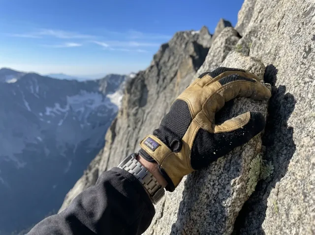 mountaineering-gloves-scrambling-hero Close-up of a scrambler's gloved hand gripping a granite hold during a Class 4 ridge scramble in alpine sunlight