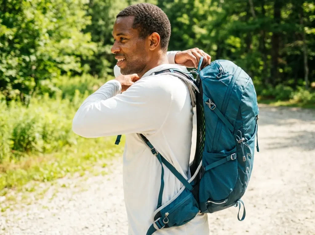 Hiker adjusting the suspended mesh back panel of an Osprey pack at a humid trailhead to maximize airflow on the spine