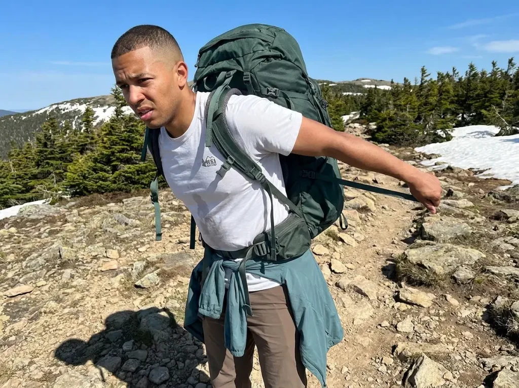 Hiker adjusting hip belt on poorly balanced backpack leaning backward on trail