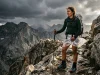 Rain Pants vs Rain Skirt for Hiking? The Safety Matrix Female hiker bracing against wind on a dark ridge wearing a translucent Zpacks DCF rain skirt and using trekking poles