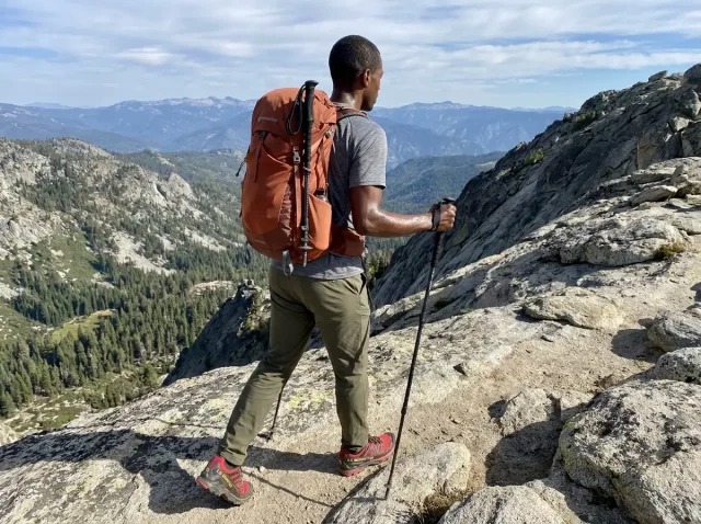 single-trekking-pole-alpine-trail-hiker Hiker using a single trekking pole on a rocky alpine trail with mountain views