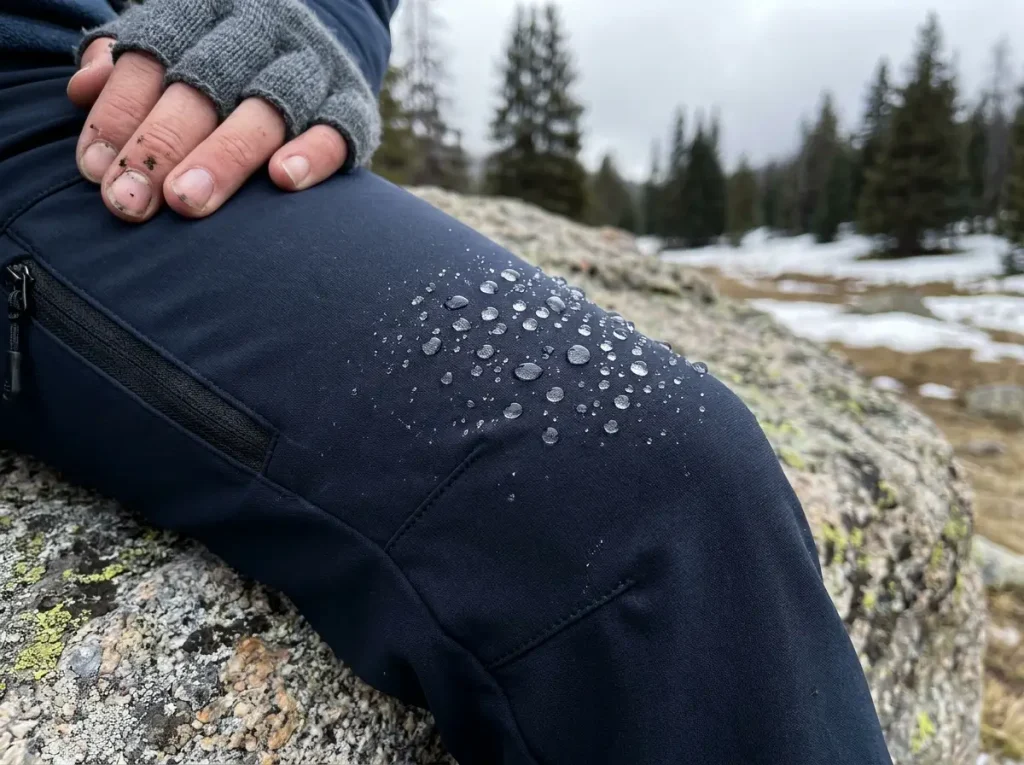 Close-up of softshell hiking pants fabric showing DWR water beading on trail