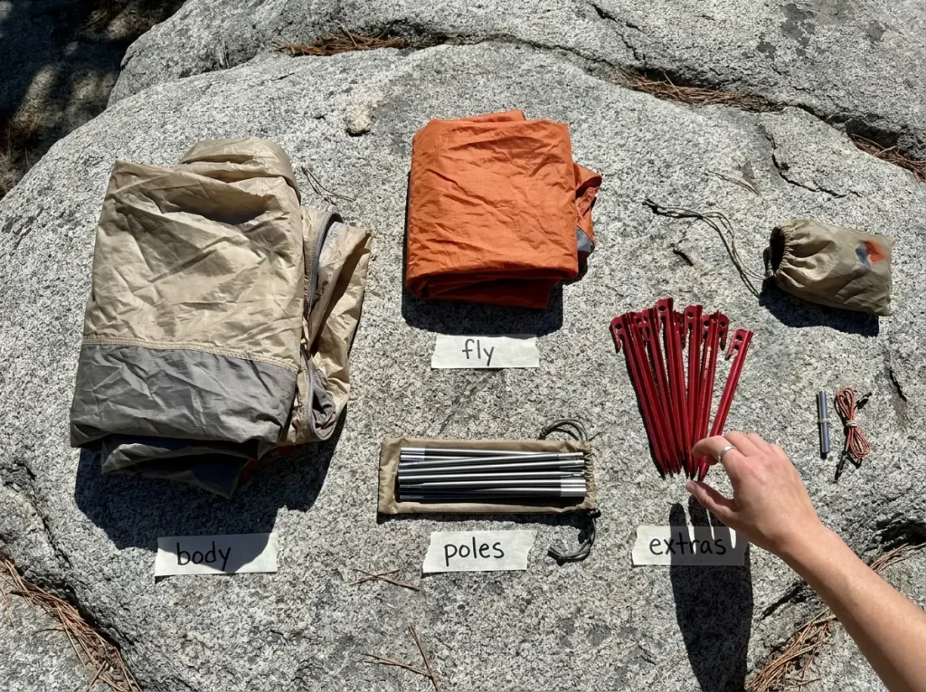 Tent components laid out separately on a flat rock showing body fly poles and stakes