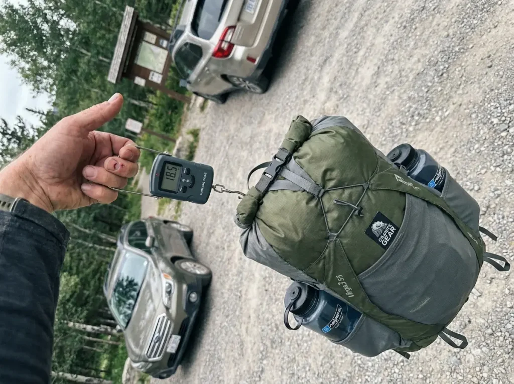 Granite Gear Virga3 55 ultralight backpack hanging from a handheld luggage scale on a trail