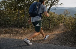 7 Road-to-Trail Shoes That Hold Up Under a Daypack Hiker in road-to-trail shoes stepping off pavement onto a dirt trail with a daypack on