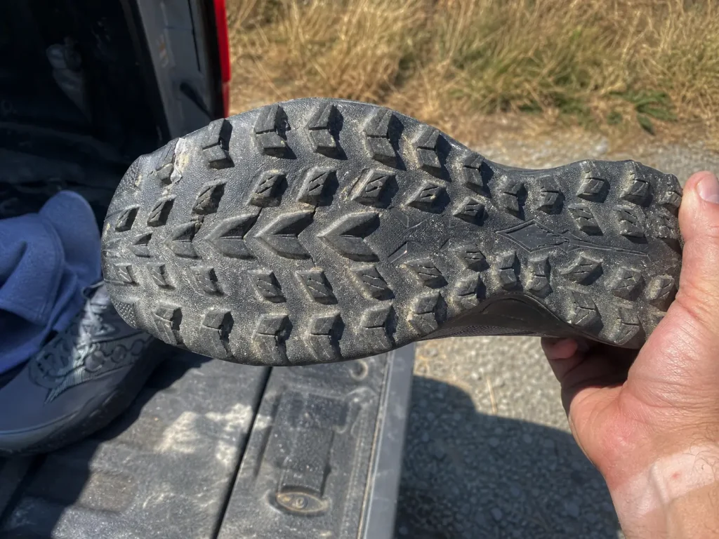 Close-up of road-to-trail shoe outsole lugs held up for inspection at a trailhead