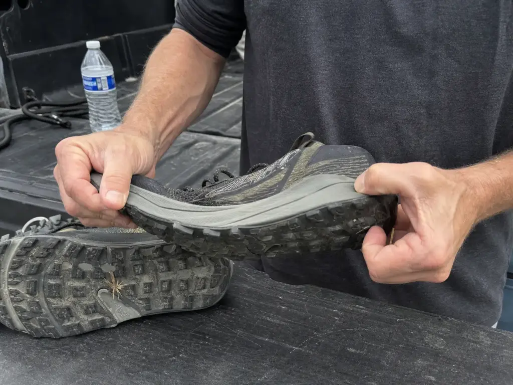 Hands twisting a trail shoe midsole to check for a rock plate before a hike