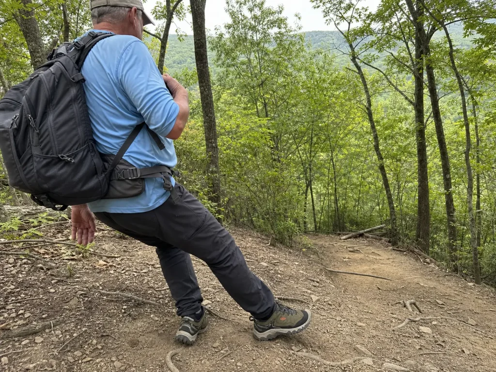 Loaded day hiker in low-cut hiking shoes stepping onto an off-camber dirt shoulder