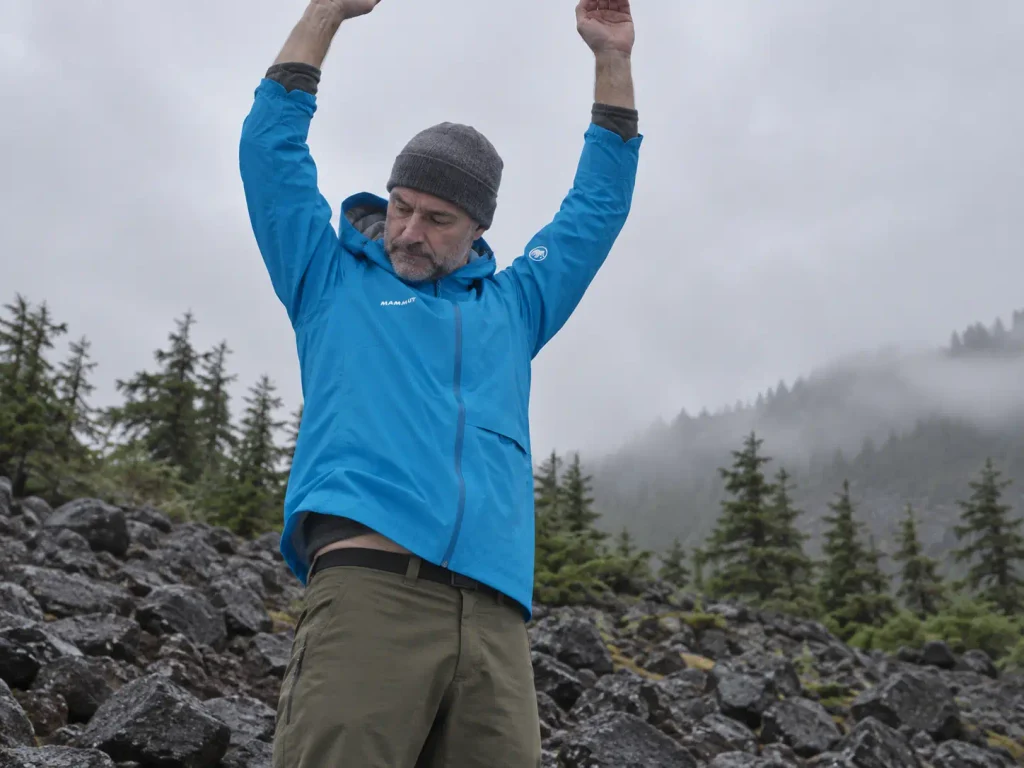Hiker reaching overhead in a rain jacket to check hem lift and sleeve length over layers
