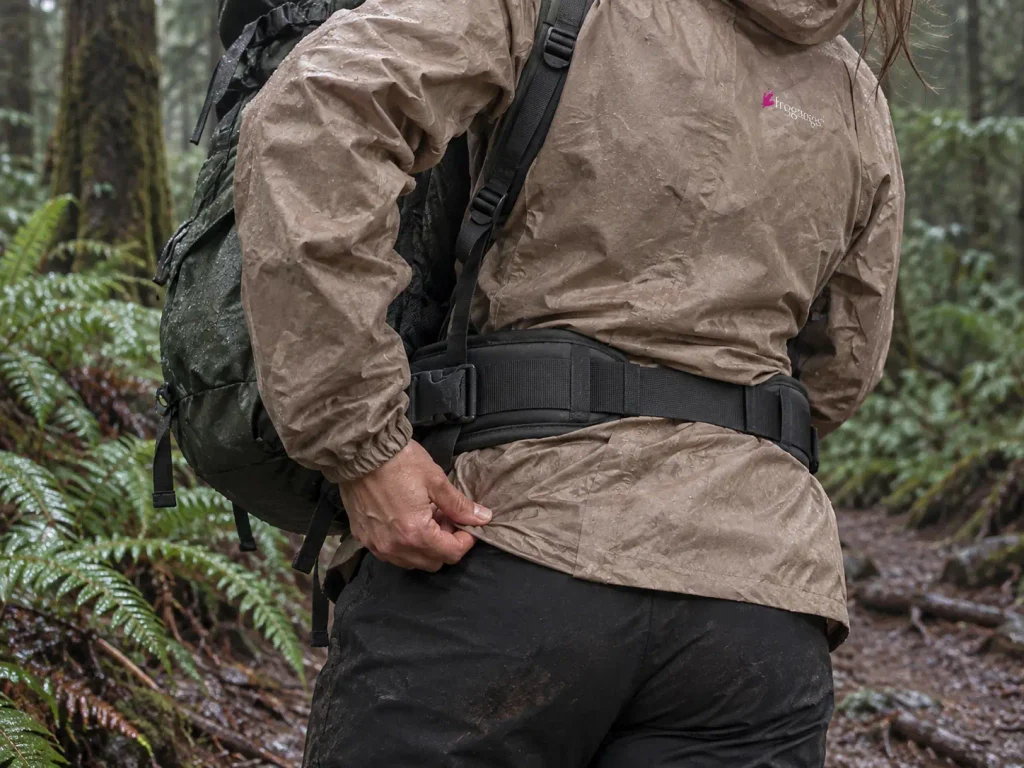 Loaded pack hip belt sitting over a rain jacket hem, the contested fit zone for layering