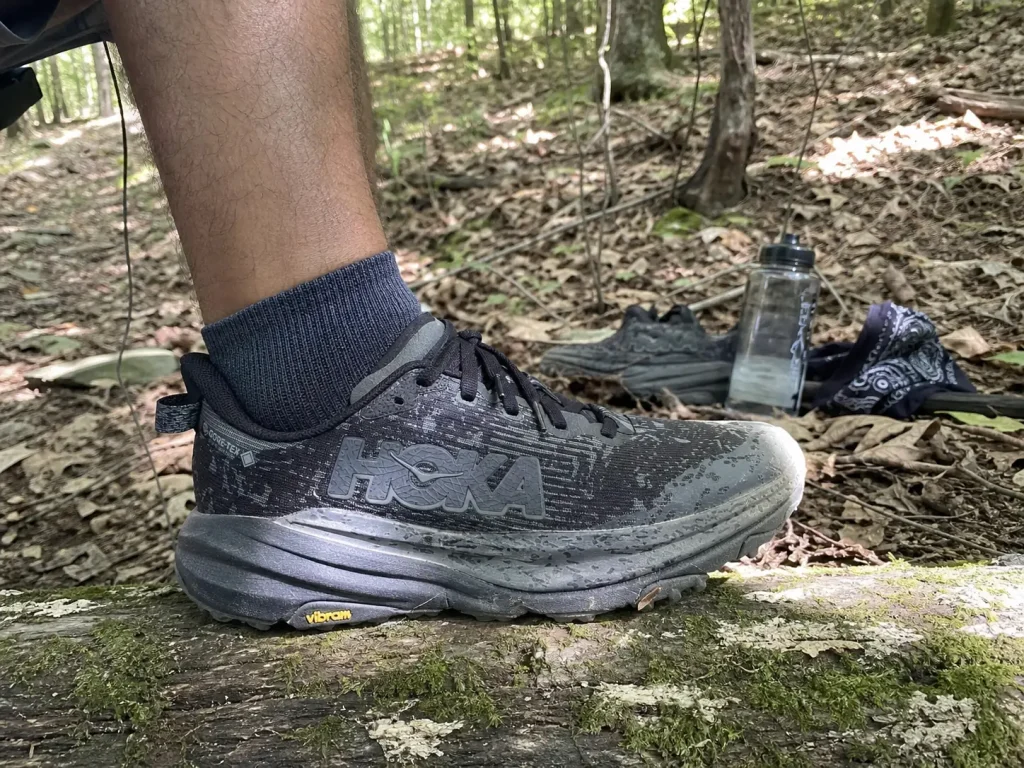 Side profile of a high stack height cushioned road-to-trail shoe on a trailside log