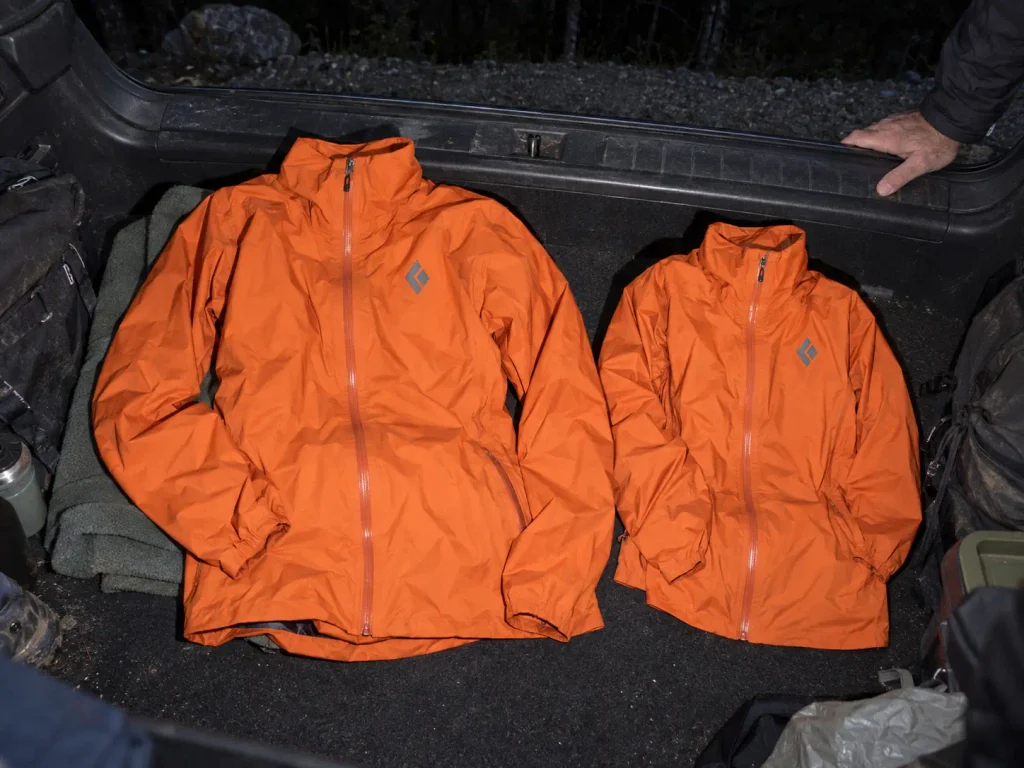 Two rain jackets in different sizes laid out in a car boot before a cold weather hike