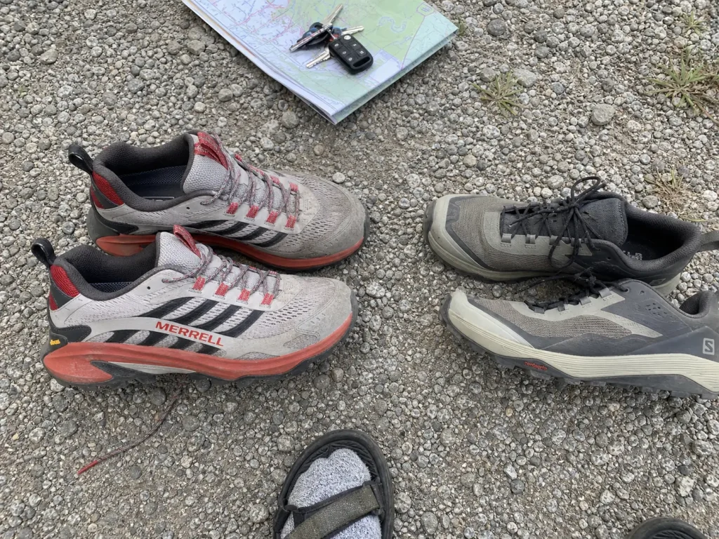Hiking brand and running brand road-to-trail shoes side by side on a gravel lot
