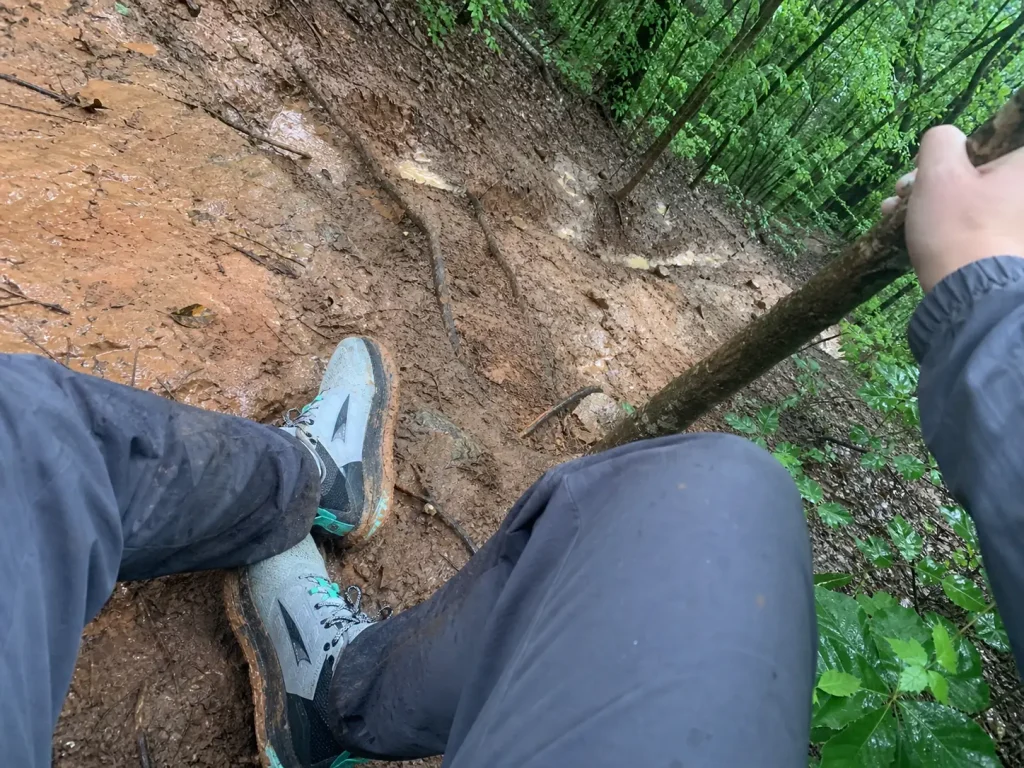 Shallow lug hiking shoes clogged with wet clay on a steep muddy trail descent