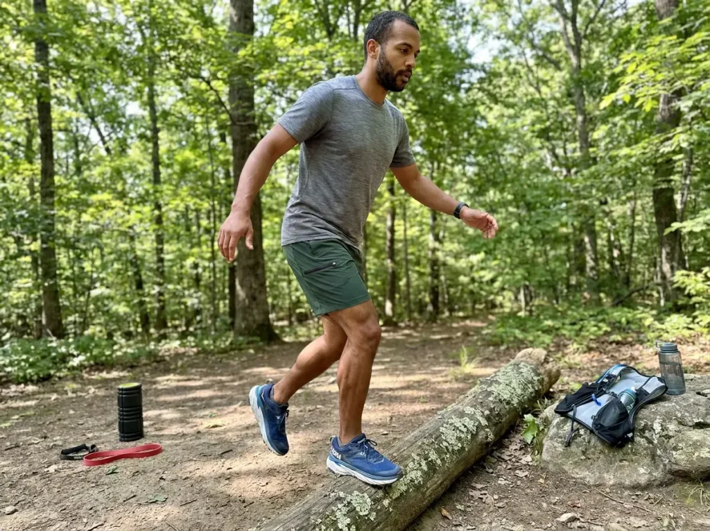 Trail runner doing ankle strengthening exercise on a log beside the trail
