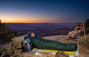 After 200 Nights Out This Is When I Skip the Tent Hiker sleeping in a sleeping bag under open stars on a desert ridge at dusk