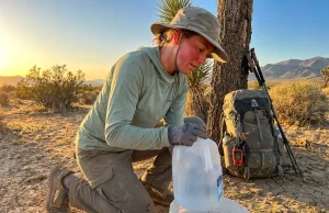 After 3 Desert Thru Hikes Here’s My Cache Plan Hiker filling water bottles from a hidden desert cache at sunrise