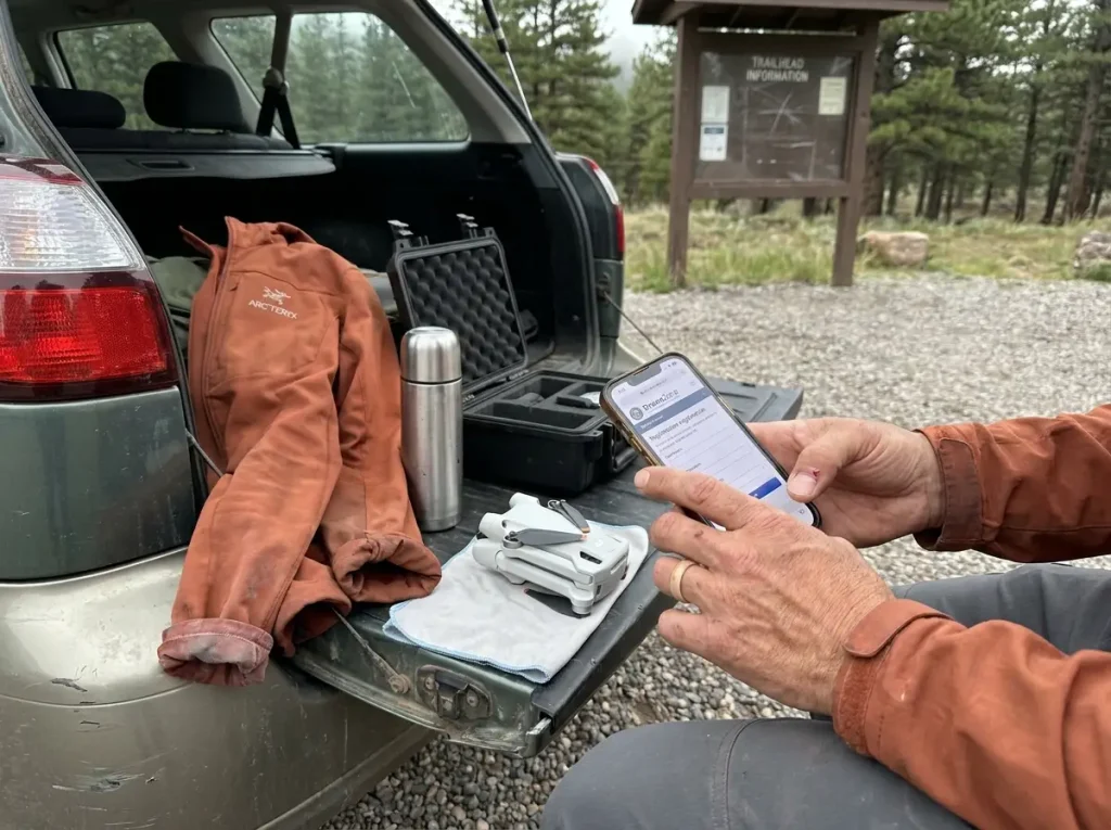 Close-up of hands registering a recreational drone on a phone at a trailhead parking lot