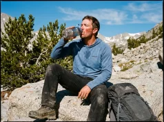 Hydration Mistakes at High Altitude Most Hikers Make Exhausted hiker drinking from water bottle on a high altitude rocky ridge