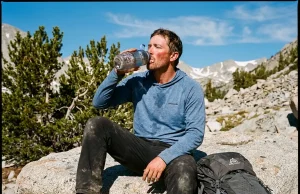 Hydration Mistakes at High Altitude Most Hikers Make Exhausted hiker drinking from water bottle on a high altitude rocky ridge