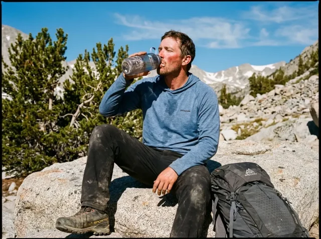 hiker-drinking-water-high-altitude-ridge Exhausted hiker drinking from water bottle on a high altitude rocky ridge