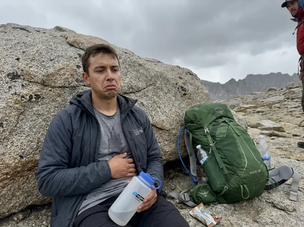 Hiker with nausea symptoms resting against a rock at high elevation