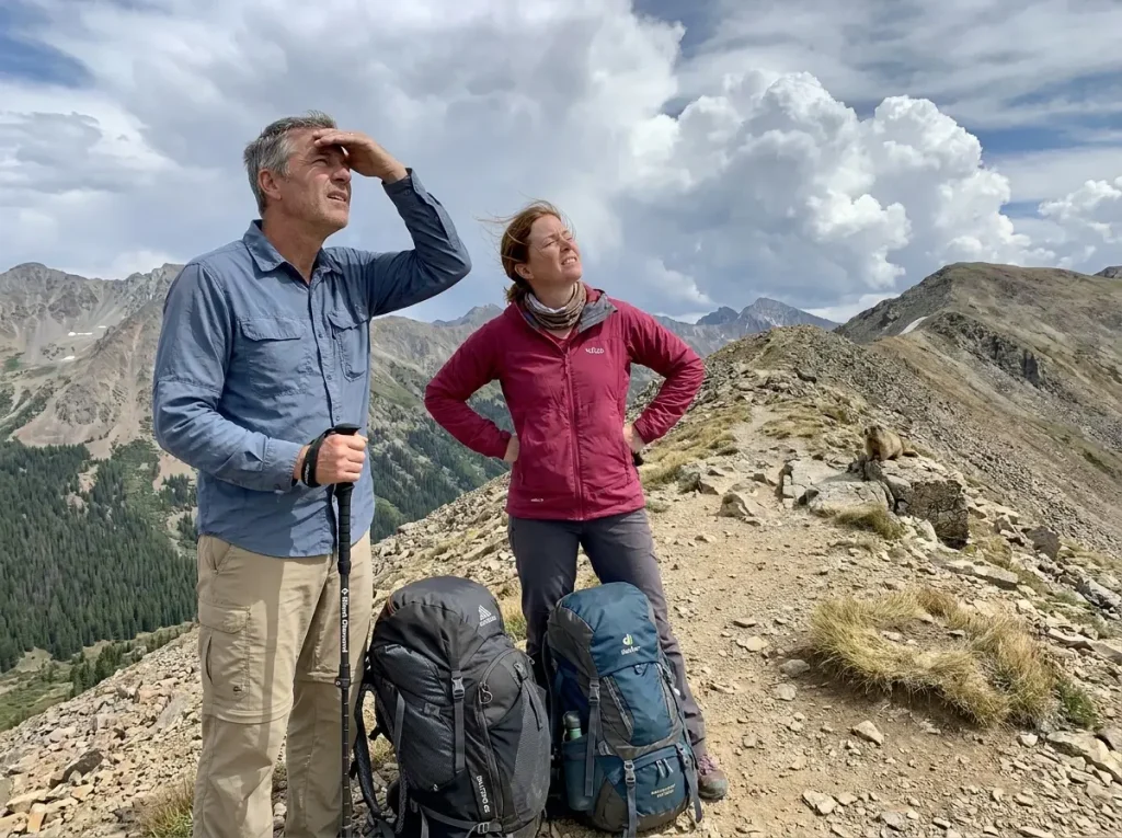 Two hikers looking up at sky on a mountain trail with concerned expressions