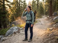 5 Hiking With Asthma Mistakes That Ruin Trips Hiker pausing on a mountain trail to use a rescue inhaler with mountain backdrop