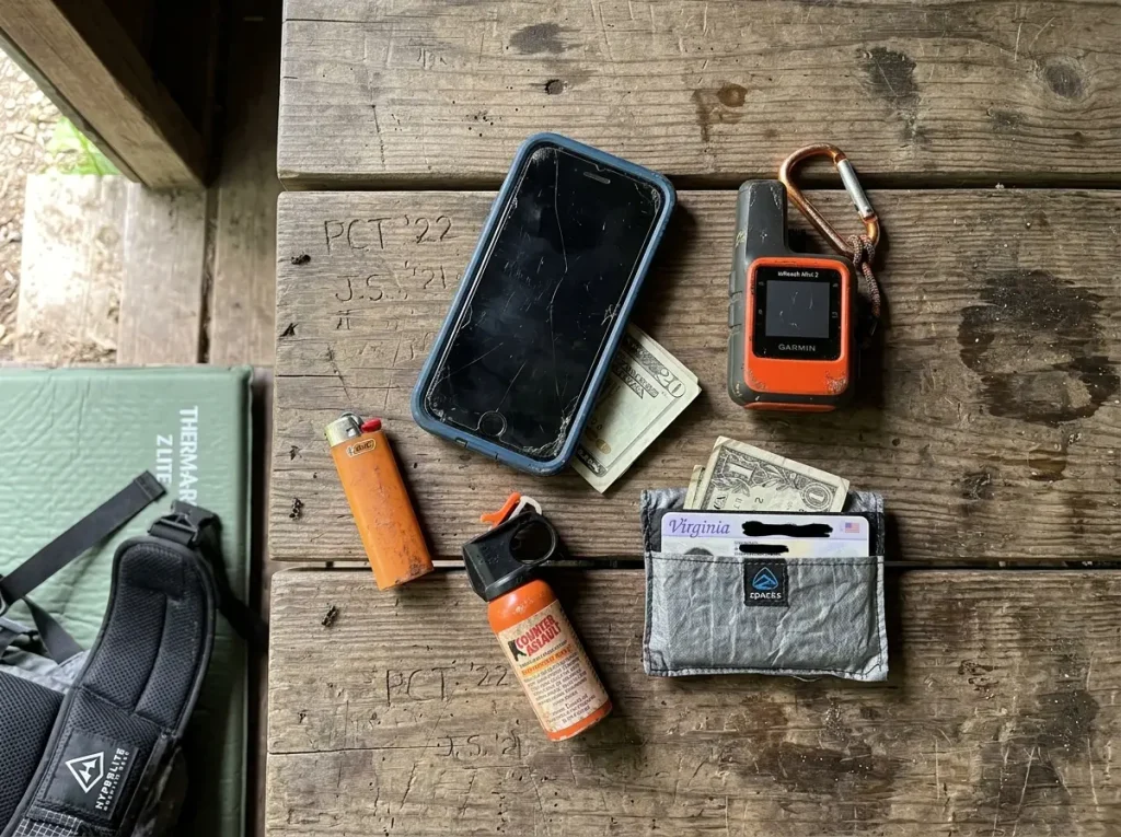 Hiker's pocket contents laid out showing phone PLB ID pepper spray
