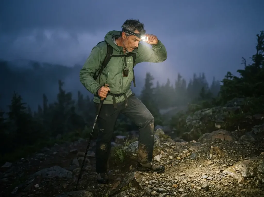 Hiker pausing on dark trail looking uncertain with headlamp beam cutting through fog