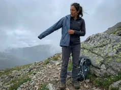 4 Rain Jacket Sizing Mistakes That Leave You Cold Hiker layering a rain jacket over fleece midlayer on a misty mountain trail