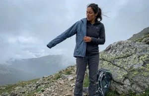 4 Rain Jacket Sizing Mistakes That Leave You Cold Hiker layering a rain jacket over fleece midlayer on a misty mountain trail