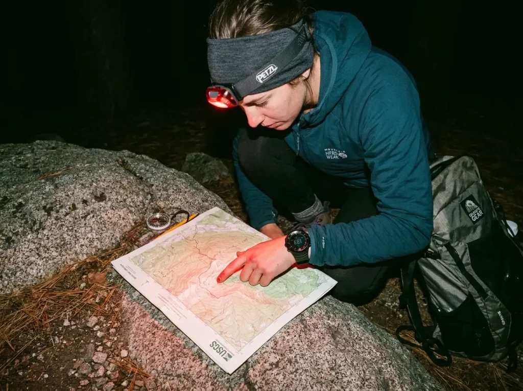 Hiker reading topographic map by red headlamp light on a dark trail
