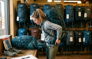 Why Buying Hiking Gear First Is a Rookie Mistake Hiker examining rental backpack fit at an outdoor gear shop counter