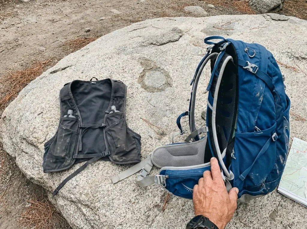 A running vest and an Osprey daypack laid side by side on granite showing their size difference