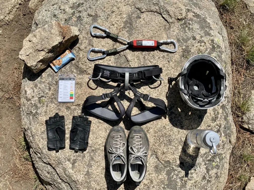 Via ferrata gear laid out on rock including harness lanyard helmet and gloves