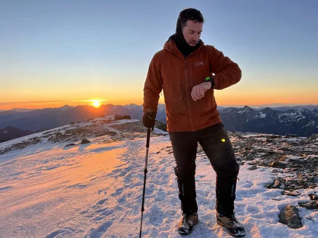 Hiker checking watch on exposed winter ridge with fading daylight