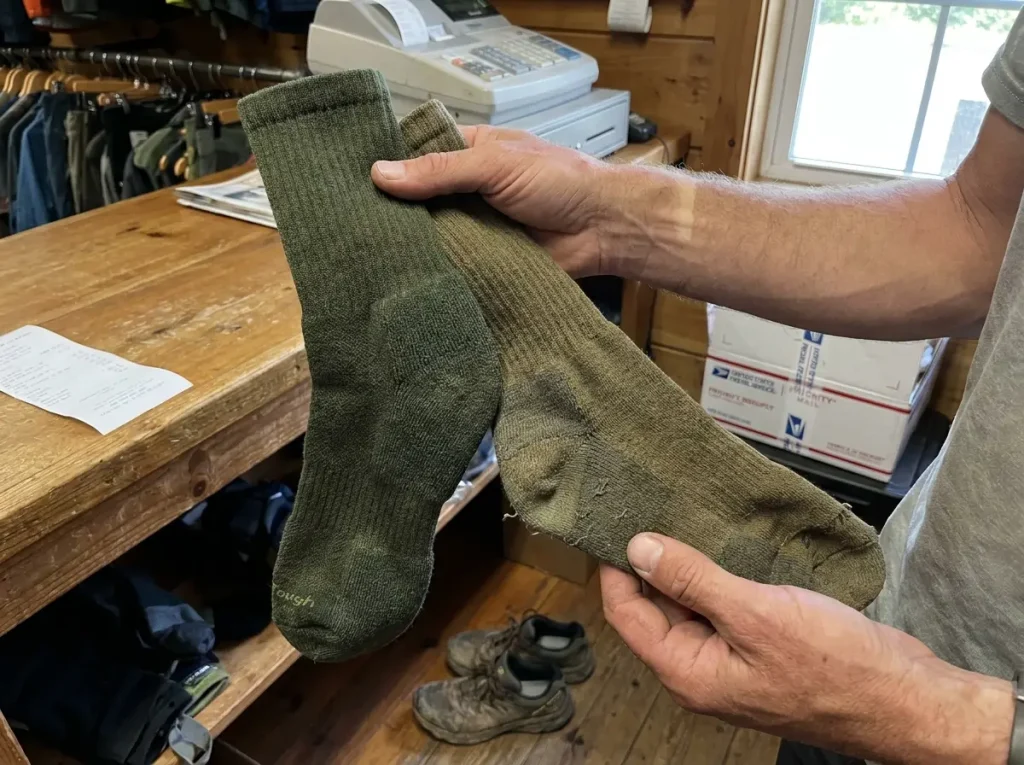 Worn out hiking sock next to new replacement sock showing wear comparison