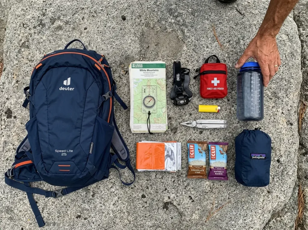 The 10 essentials laid out beside a lightweight daypack on a granite slab before a day hike