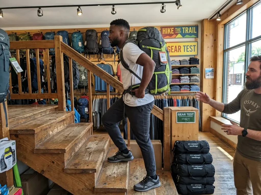 Hiker load-testing a weighted hiking backpack on stairs inside an outdoor gear shop