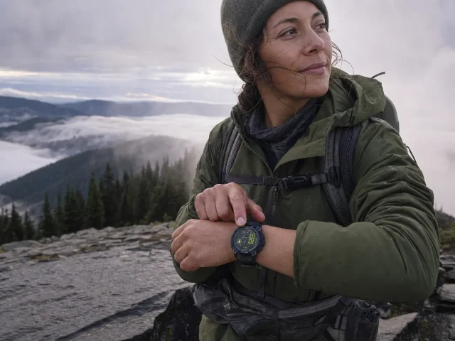 0-best-gps-watch-hiking-hero-wrist-overlook Day hiker checking a Garmin GPS watch on the wrist at a misty overlook on a cool morning