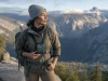 Best Hiking Apps and Maps and When They Fail Hiker at an overlook checking a phone mounted on a chest strap with a paper map tucked in the pack lid