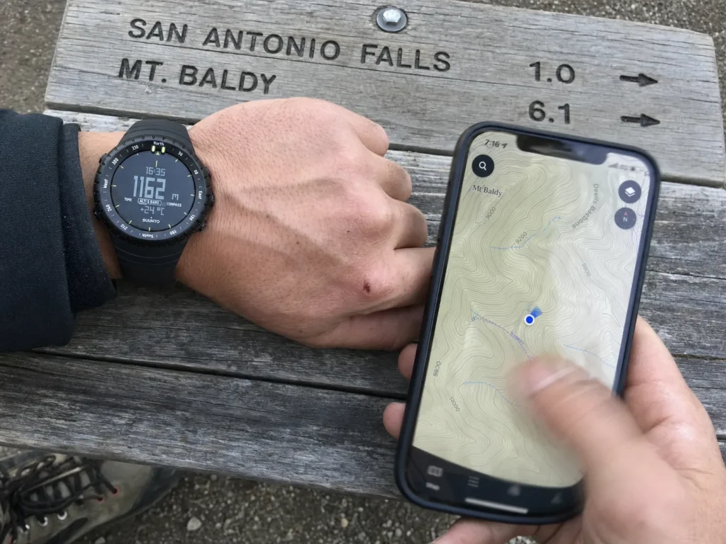 Hiker comparing a phone map app against an ABC watch at the trailhead to decide on GPS